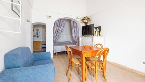 Una habitación compacta con cama, una mesa de comedor con sillas, televisión y una pequeña cocina americana.