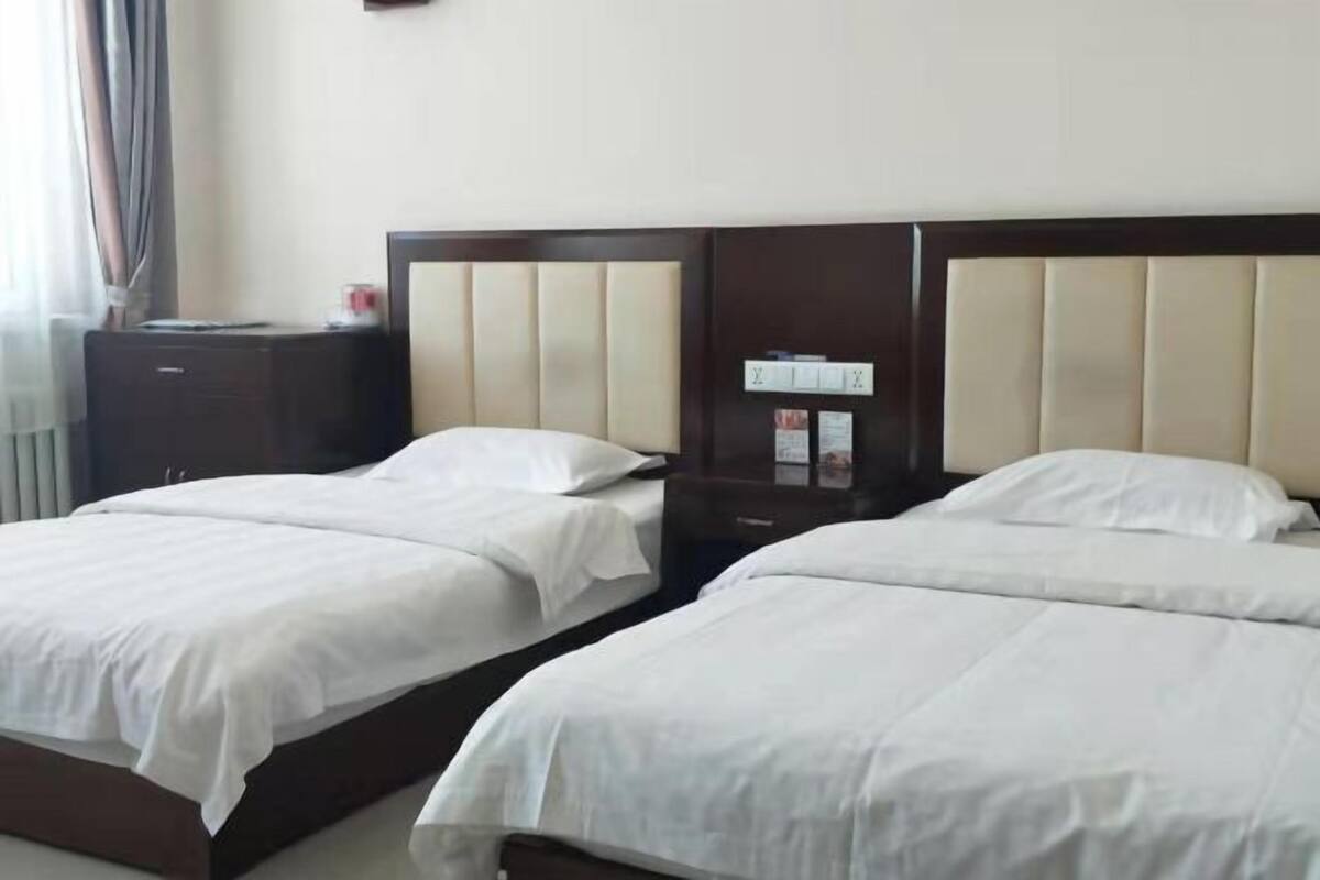 A hotel room with two beds, a nightstand, and a small cabinet.