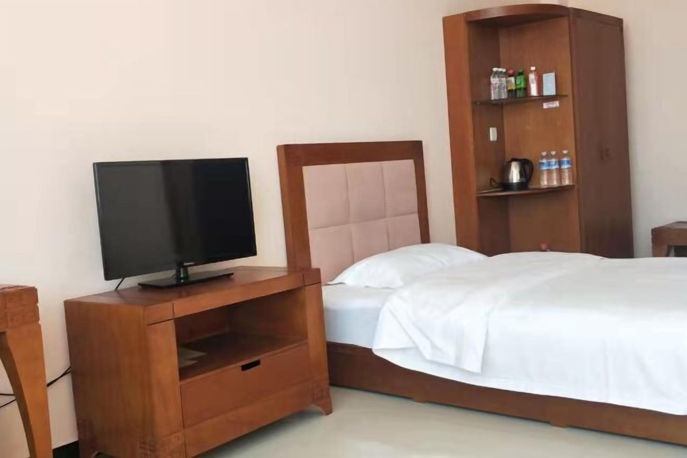 Una camera d'albergo con un letto di legno, una TV su un mobiletto in legno e uno scaffale a incasso con articoli da toilette.