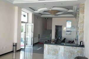 Zona de recepción de un hotel con mostrador de mármol, una escalera y un candelabro.