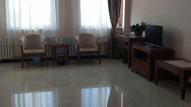 A living room with two armchairs, a small table, a television on a wooden stand, and a radiator. - Zhenglan Qijiatai Business Hotel (Zhenglan Banner)