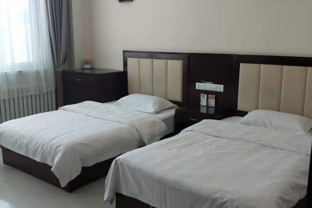 A hotel room with two beds, a nightstand, and a window with curtains.