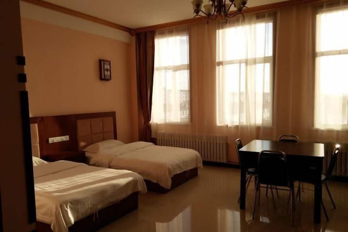 A hotel room with two beds, a dining table, and a chandelier.