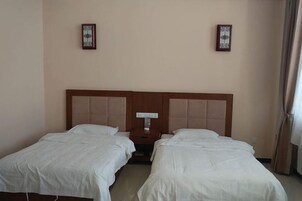 Habitación de hotel con dos camas individuales, una mesita de noche y una lámpara fijada a la pared.