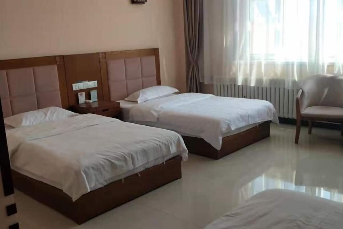 A hotel room with two beds, a wooden headboard, a nightstand, a chair, and a window with curtains.