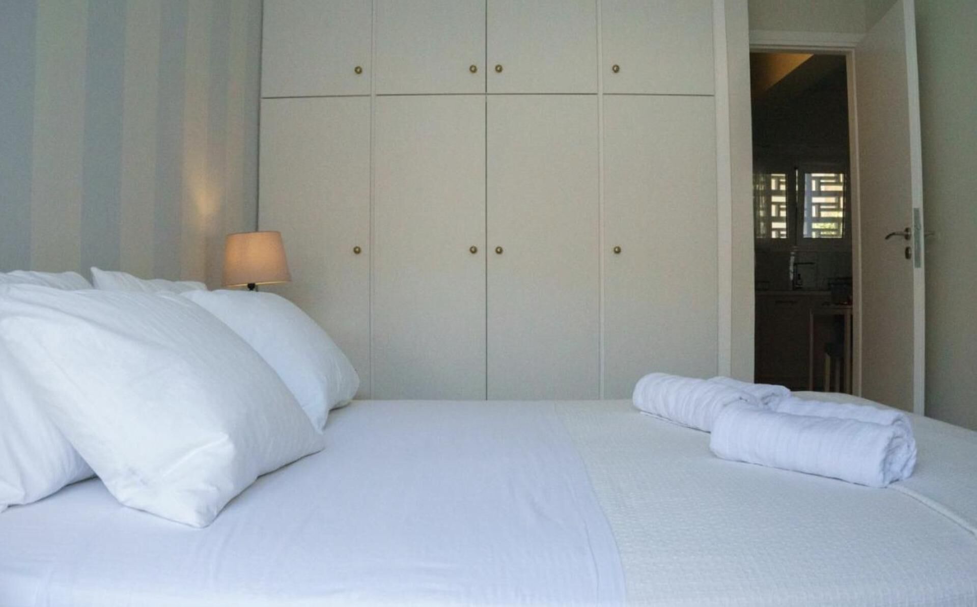 Un lit bien fait, avec du linge de lit blanc et des oreillers, une lampe de chevet et une armoire à deux portes.
