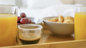 Una bandeja de desayuno con jugo de naranja, una taza pequeña de café, un bol de croissants y un plato de uvas rojas.