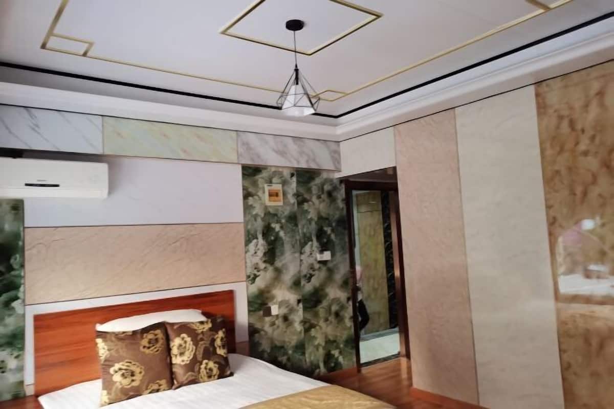 A bedroom with a bed, a headboard, a ceiling light fixture, and a wall with a patterned design.