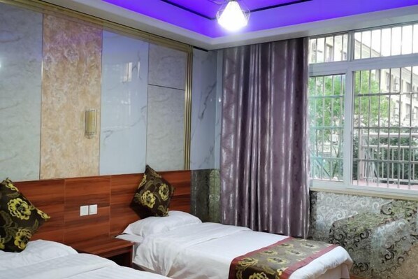Habitación de hotel con cabecera de madera, dos camas con almohadas estampadas con motivos florales, una ventana con cortinas y vistas a zonas verdes.