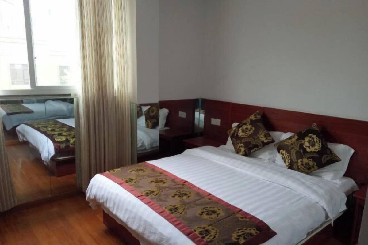 A hotel room with a bed, a bedside table, a mirror, and a window with curtains.