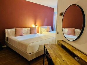 Quarto de hotel com duas camas, uma secretária de madeira e um espelho grande na parede.