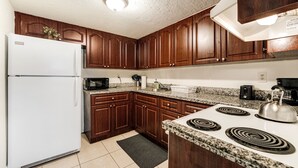 A kitchen with wooden cabinets, a white refrigerator, a microwave, a stove, and granite countertops. - Comfortable 3-bedroom apartment with easy access to major highways (MIAMI)