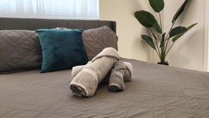 A neatly made bed with a quilted bedspread, two pillows, and rolled towels on a room with a large window and a potted plant. - Comfortable 3-bedroom apartment with easy access to major highways (MIAMI)