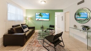 A living room with a glass coffee table, leather sofa, and a TV displaying a beach scene. - Comfortable 3-bedroom apartment with easy access to major highways (MIAMI)