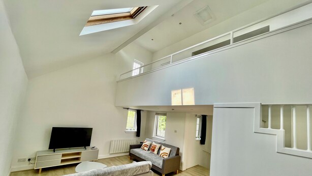 A spacious living area with a high ceiling, a sofa, a TV, and a staircase leading to an upper level. - 17th Century Dovecot, 20 min to Edinburgh by train (Inverkeithing)