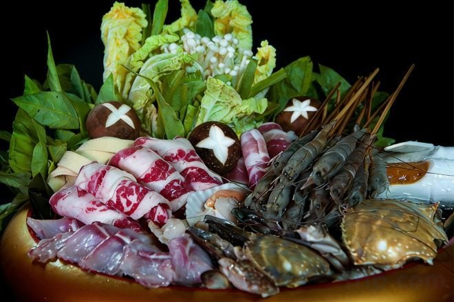 Un plateau de fruits de mer comprenant différents types de fruits de mer, notamment des crevettes, du crabe et du calmar, disposés sur un lit de verdure et de fleurs.