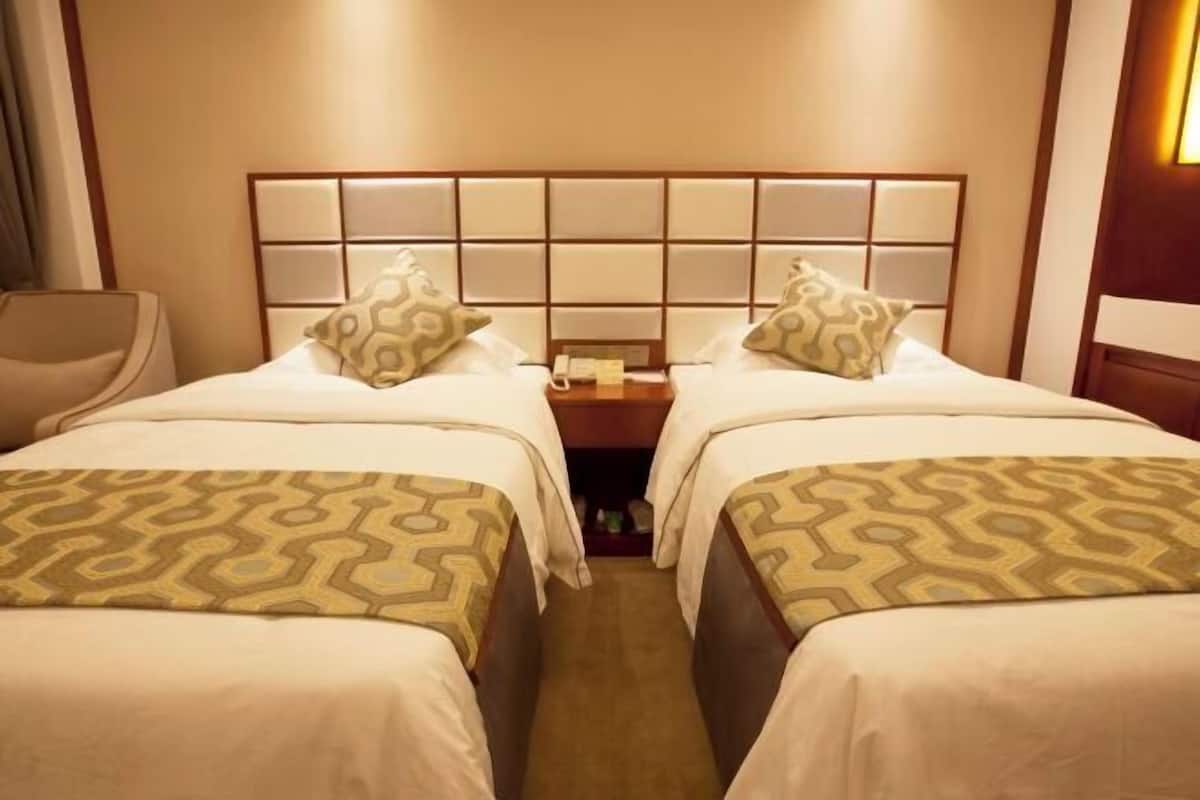 A hotel room with two beds, a nightstand, a chair, and a headboard with a light panel.