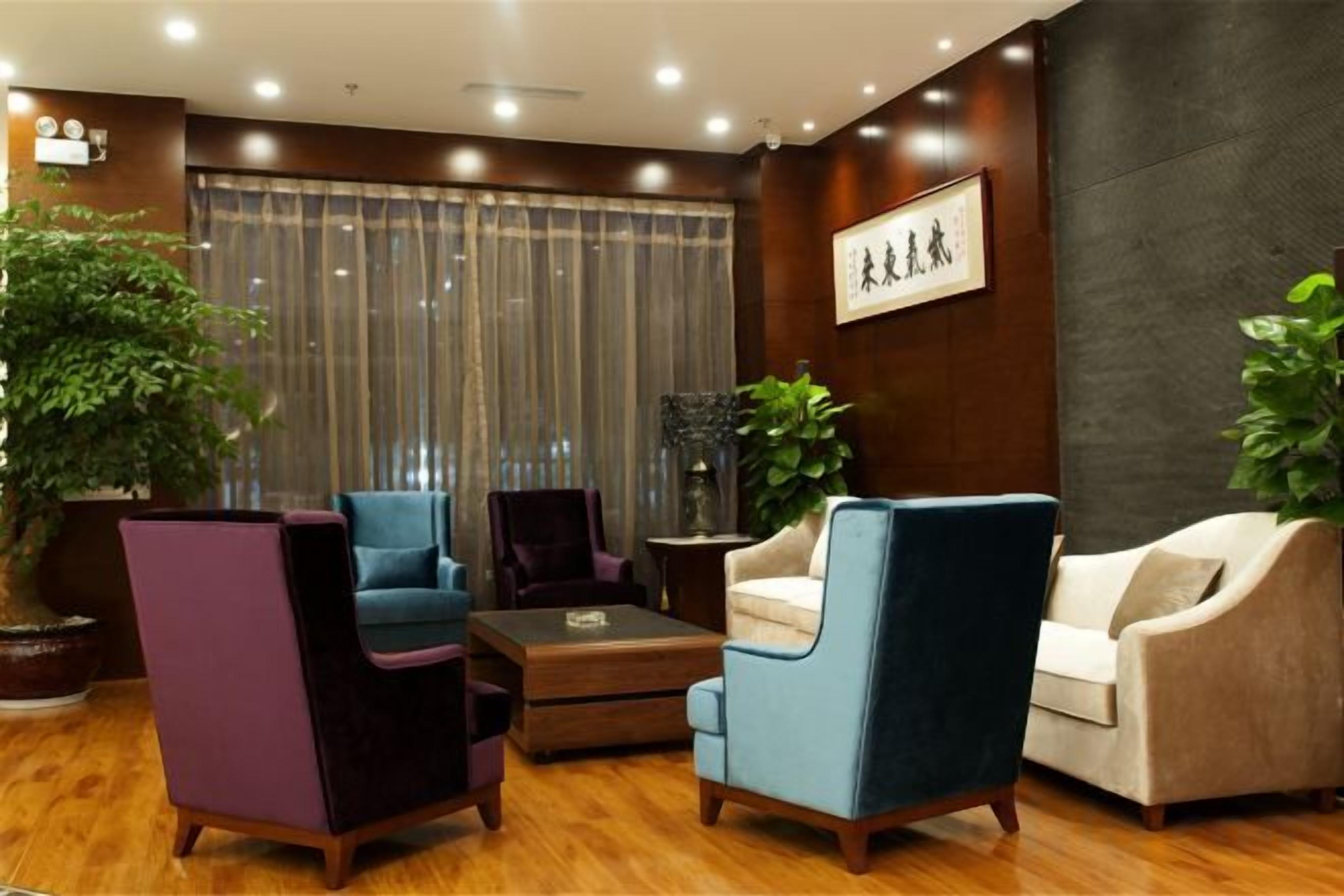 Una habitación con piso de madera, una planta grande en maceta y una zona de estar con dos sillones y un sofá.