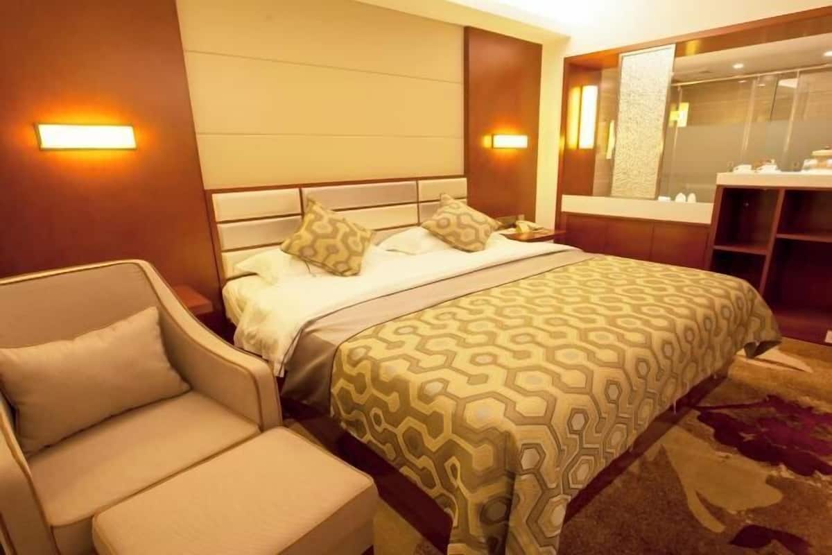 A hotel room with a bed, a sofa, a nightstand, a mirror, and a bathroom area.