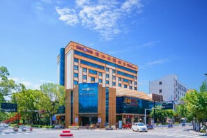 A multi-story hotel with a prominent entrance, large windows, and a clear blue sky. - Chengjiang Manor Hotel (Chengjiang)