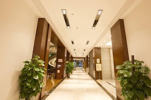 A hotel corridor with a marble floor, large potted plants, and a modern ceiling design. - Chengjiang Manor Hotel (Chengjiang)