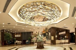 Un vestíbulo con una lámpara decorativa en el centro, arreglos de asientos y una recepción.
