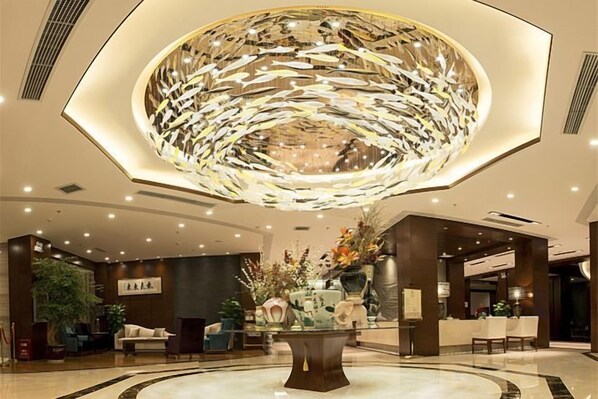 A lobby with a central decorative light fixture, seating arrangements, and a reception desk.