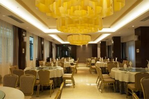 A banquet hall with round tables, chairs, and a large chandelier.