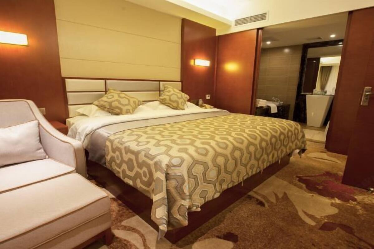 A hotel room with a bed, a sofa, a mirror, and a bathroom visible through an open door.