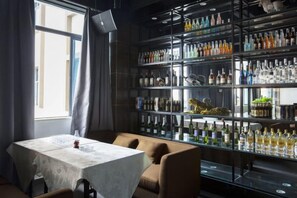 Eine Bar mit Tischen und Stühlen, eine große Glasvitrine mit Flaschen sowie ein Fenster mit Vorhängen.