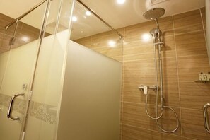 Cabina de ducha con paredes de vidrio, cabezal de ducha de mano y grifo empotrado.