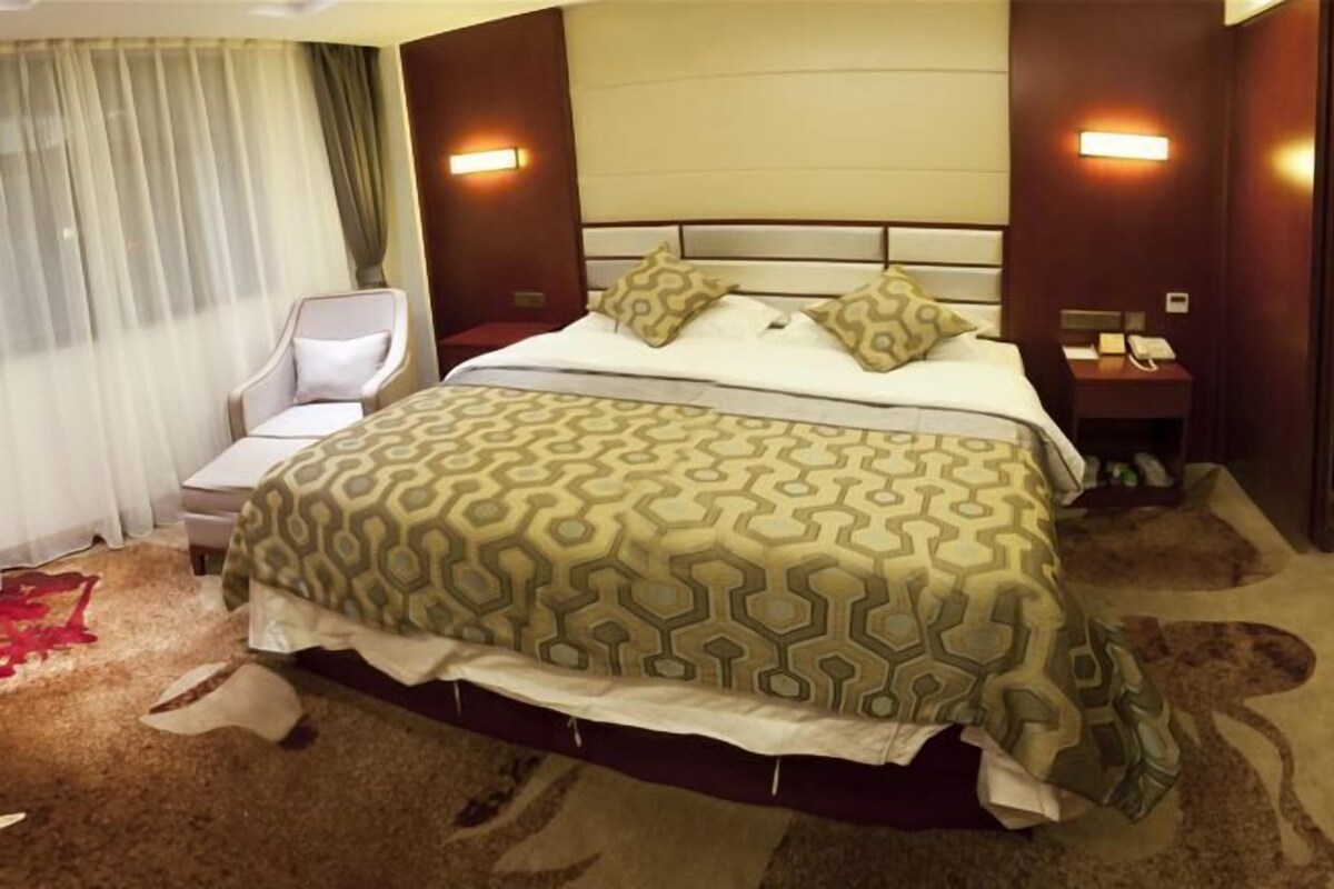 A hotel room with a large bed, a chair, a nightstand, and a lamp.