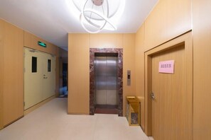 Un couloir d’hôtel avec un comptoir d’accueil, un ascenseur et une porte avec une pancarte.