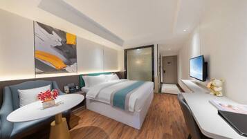 A modern hotel room with a bed, a desk, a chair, a TV, and a painting on the wall.