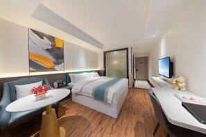 Une chambre d’hôtel moderne, équipée d’un lit, d’un bureau, d’une chaise, d’une télévision et ornée d’un tableau au mur.