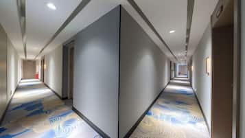 A hotel corridor with a patterned floor, doors on both sides, and a ceiling with recessed lighting.