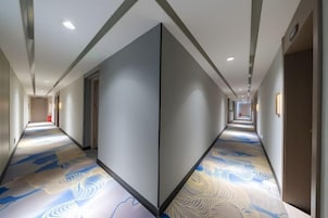 A hotel corridor with a patterned floor, doors on both sides, and a ceiling with recessed lighting.