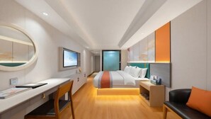 Quarto de hotel moderno com cama, escrivaninha, cadeira e televisão.