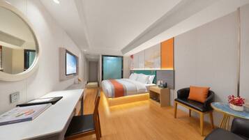 A modern hotel room with a bed, a desk, a chair, a sofa, and a small table with flowers.