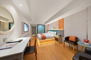 Une chambre d’hôtel moderne équipée d’un lit, d’un bureau, d’une chaise, d’un canapé et d’une petite table agrémentée de fleurs.