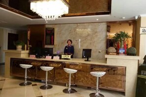 A hotel reception area with a marble counter, a receptionist, and three bar stools. - Balikun Hancheng Hotel (Barkol)