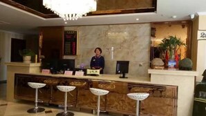 Zona de recepción de un hotel con mostrador de mármol, una recepcionista y tres taburetes de bar.