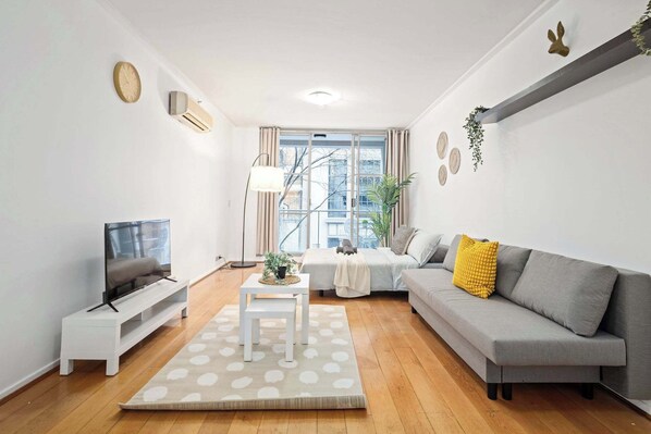 A modern living room with a sofa, TV, and a small table with a plant. - A Stylish Studio for 6, Next to Darling Harbour (Sydney)