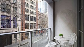 Un balcon doté d’une balustrade en verre, de deux chaises blanches et d’une petite table sur laquelle est posée une plante.
