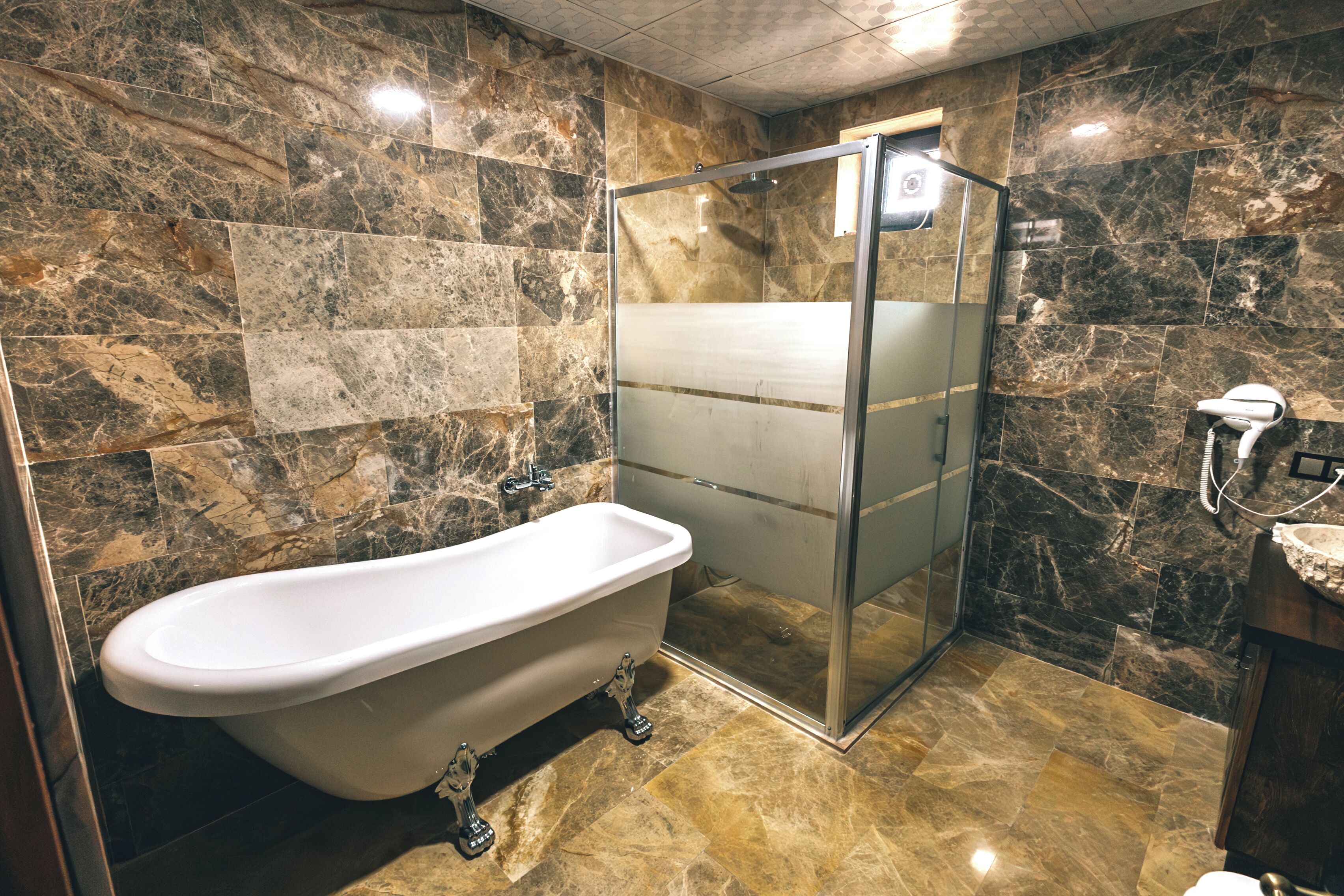 Un baño con una bañera independiente, ducha con mampara de vidrio y paredes de mármol.