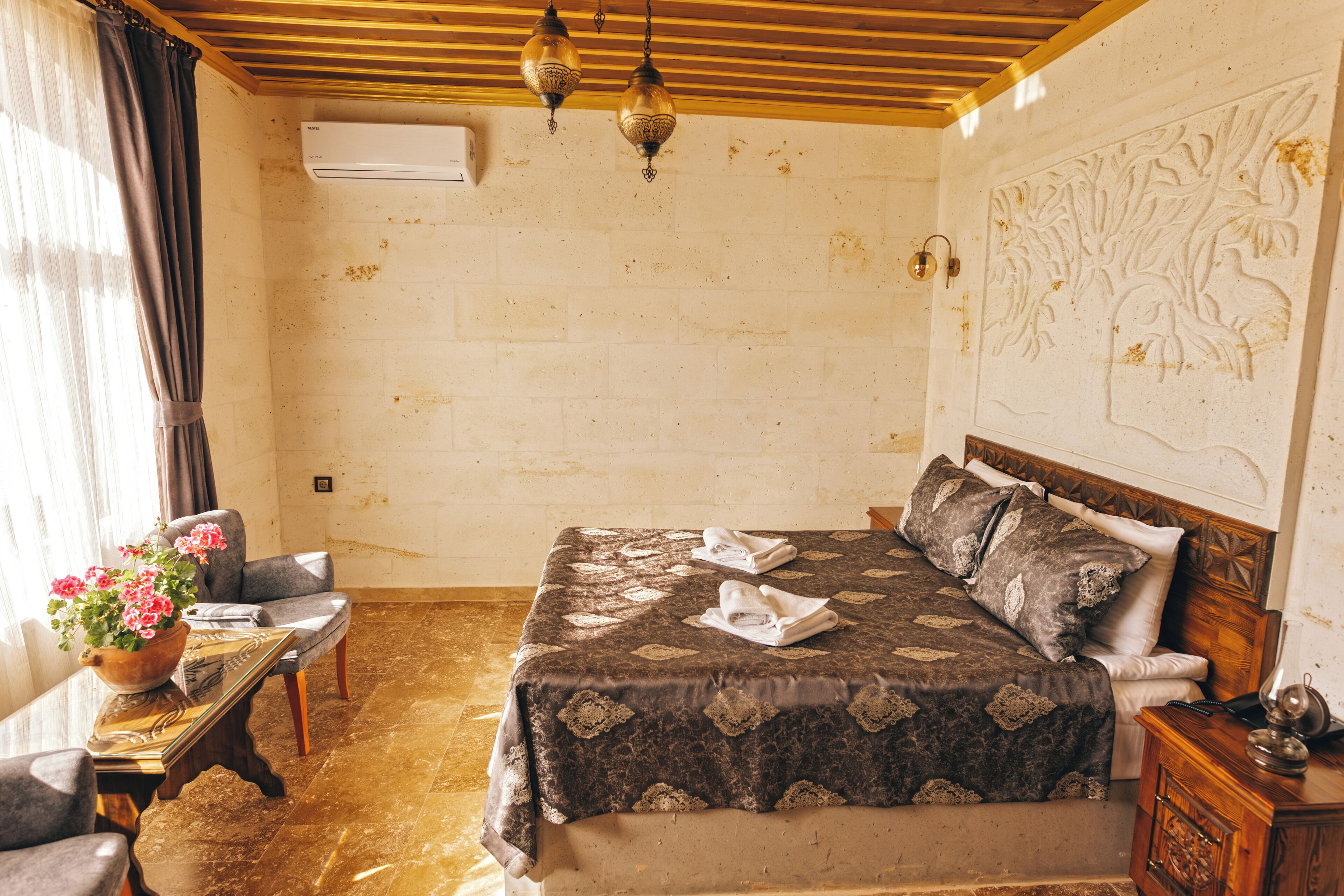 Un dormitorio con una cama, una silla, una mesa con un florero y una pared con un relieve decorativo.