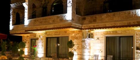 A two-story hotel with a stone facade, a covered upper level, and a well-lit outdoor area with seating.