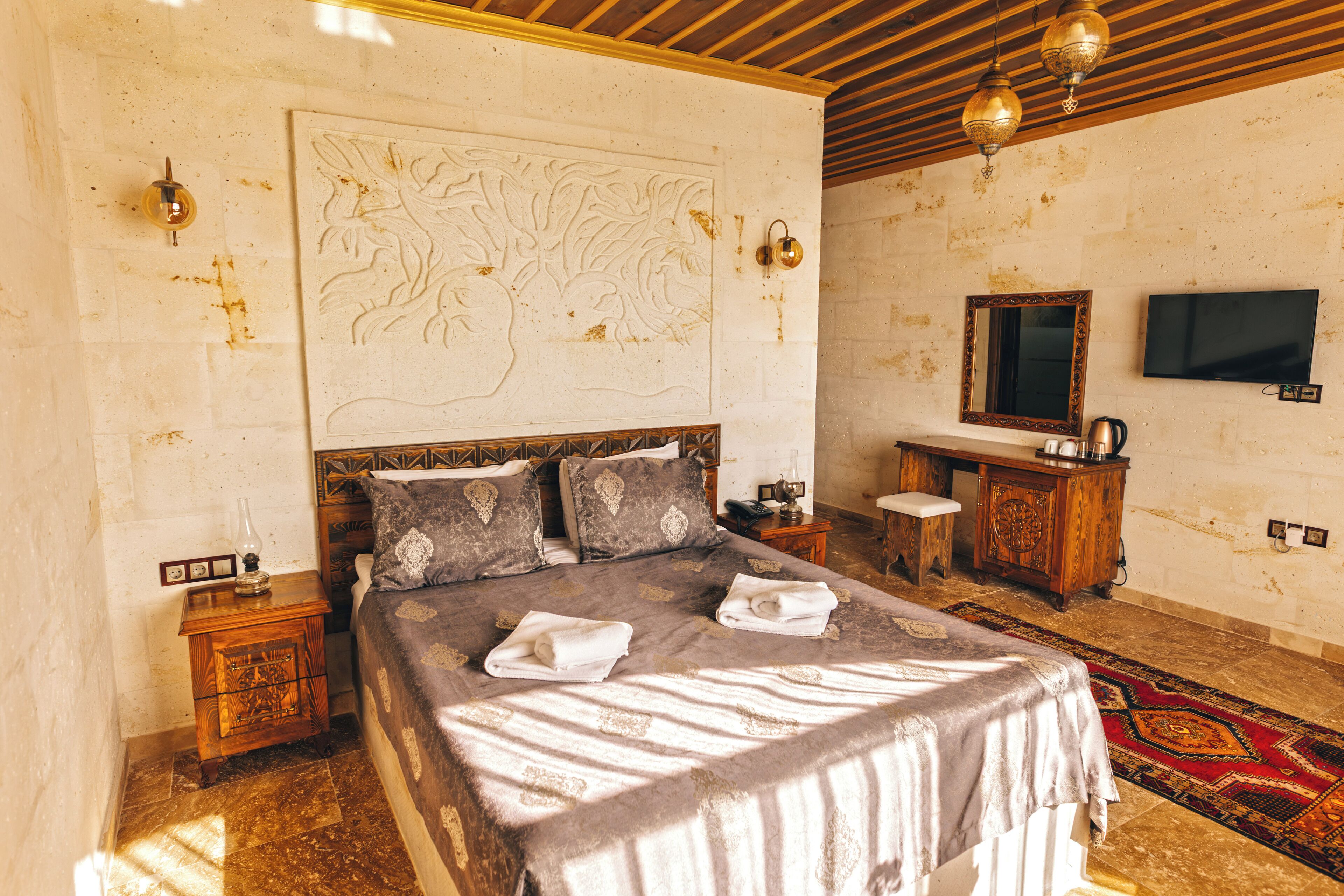 A bedroom with a large bed, a wooden headboard, a nightstand, a dresser, a television, and a decorative wall piece.