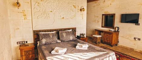 A bedroom with a large bed, a wooden headboard, a nightstand, a dresser, a television, and a decorative wall piece.