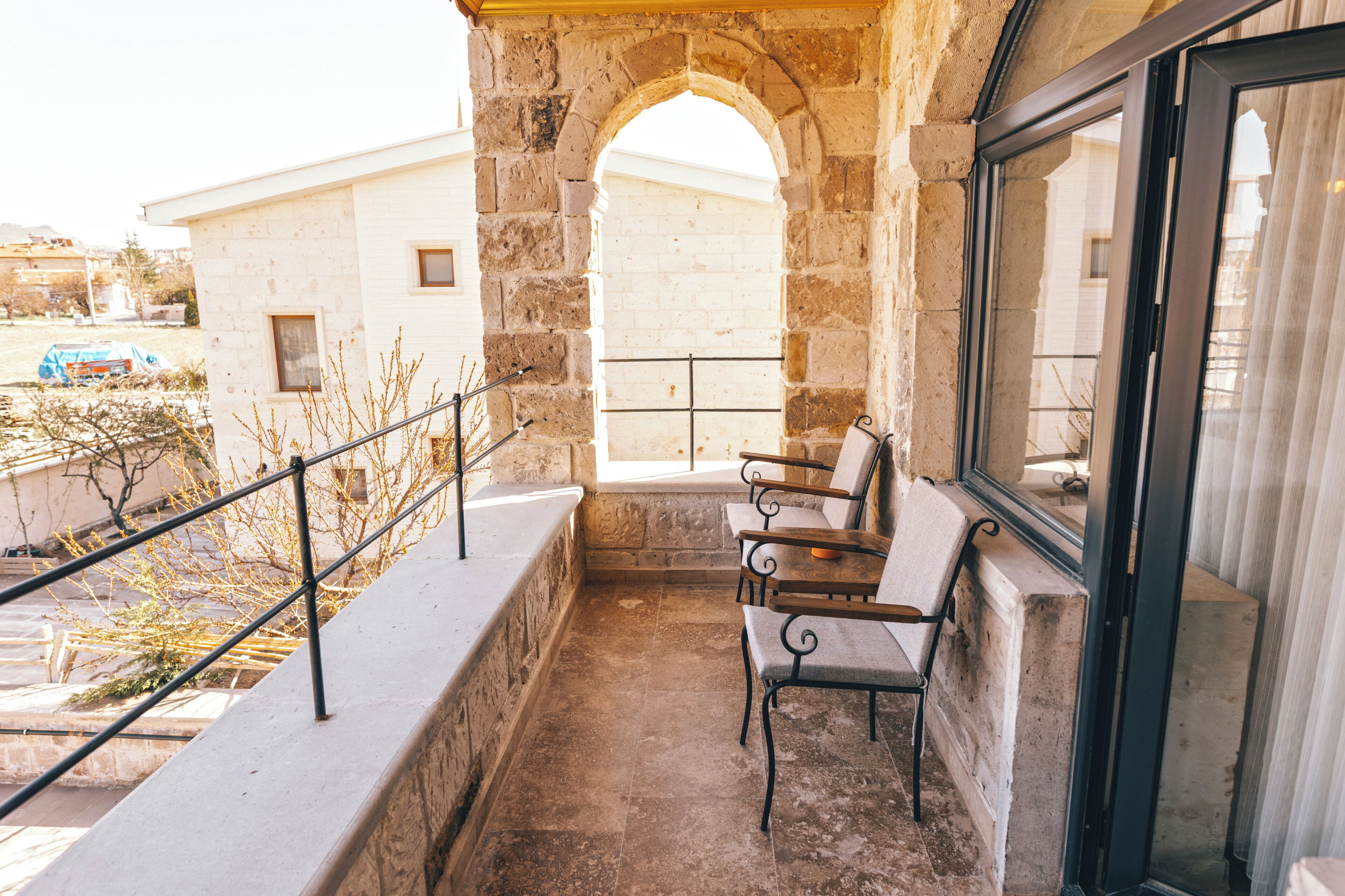 A balcony with stone walls, a metal railing, and a view of a building through an archway.